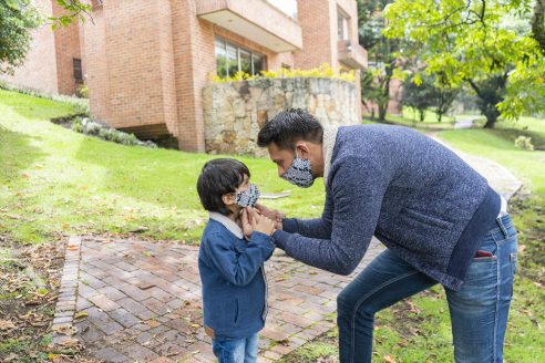 爸爸穿着拉丁裔的人平均年龄30年casually with a face mask on helps his 5-year-old son to put on his mask to avoid the spread of covid-19 both are outside his house